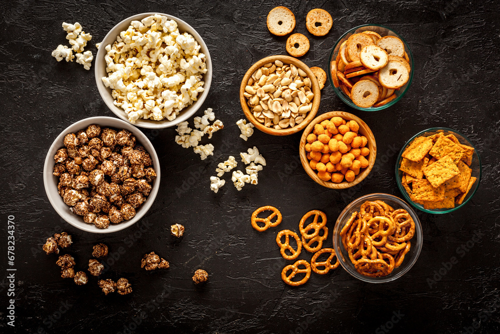 Set of many salty snacks in bowls - pretzels nuts chips top view
