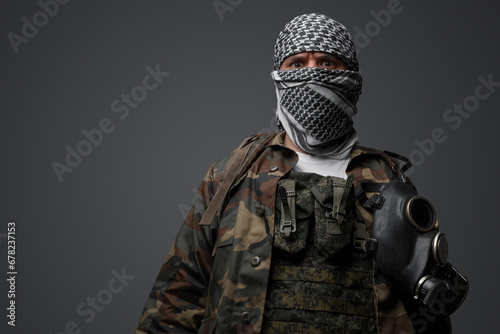 Middle Eastern radical fanatic soldier donning a white keffiyeh and camouflaged field uniform, armed with an automatic rifle, against a gray background