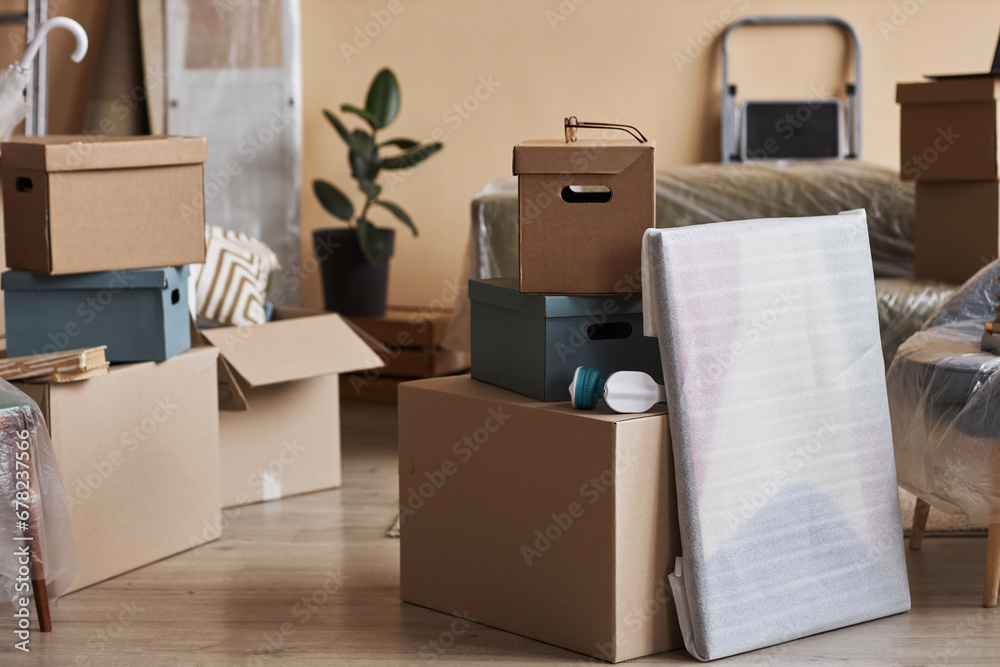 Stack of packed cardboard boxes and wrapped painting standing on the floor in the center of spacious living room of new apartment Stack of packed cardboard boxes and wrapped painting standing on the floor in the center of spacious living room of new apartment