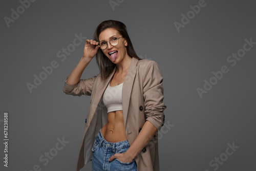 Smiling, chic lady in athletic bra and jacket radiates happiness on a gray backdrop
