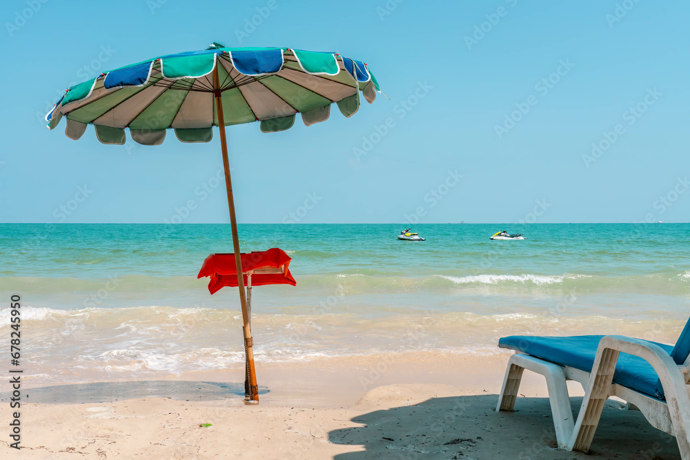 Small cafe menu table under a beach umbrella stands in front of seashore line, sun beach lounge chair, two jetski in a sea