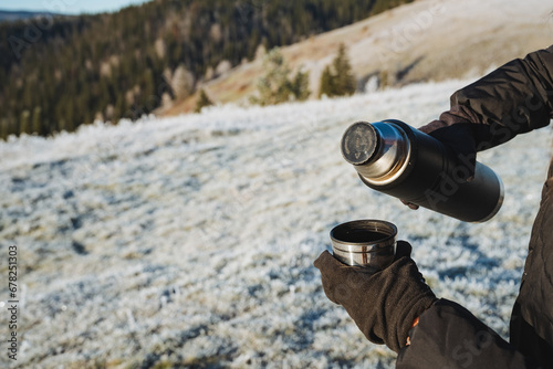 Thermos with hot tea in nature in winter, man holding mug and thermos in hands, picnic in nature.