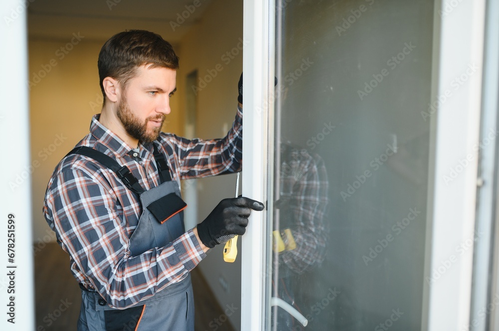 Workman in overalls installing or adjusting plastic windows in the living room at home Workman in overalls installing or adjusting plastic windows in the living room at home