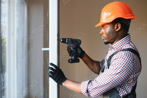 Close-up Of Young African Handyman In Uniform Installing Window