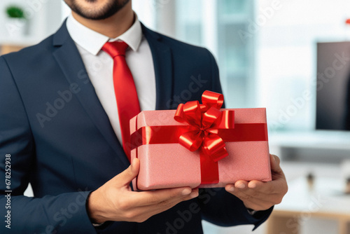 Cropped view of businessman holding gift box with red ribbon in office.