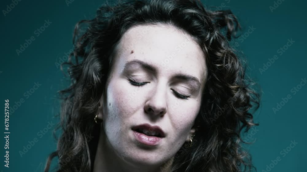 Disinterested expression of woman rolling eyes discrediting expressed views, tight close-up face of female person in 20s behind teal background