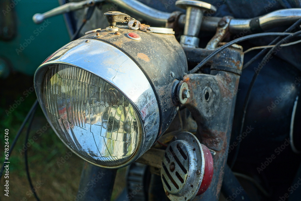 glass round large front powerful old iron chrome shiny classic electric halogen headlight with an iron steering wheel  from an old retro black  motorcycle on the street during the day
