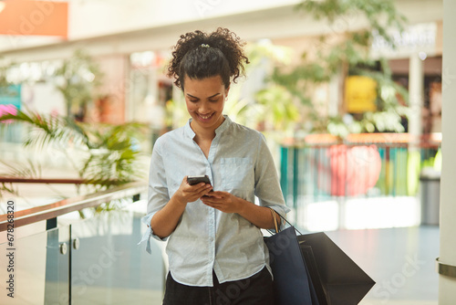 A smiling adult holds a shopping bag, using a smartphone for communication while shopping at the mall.