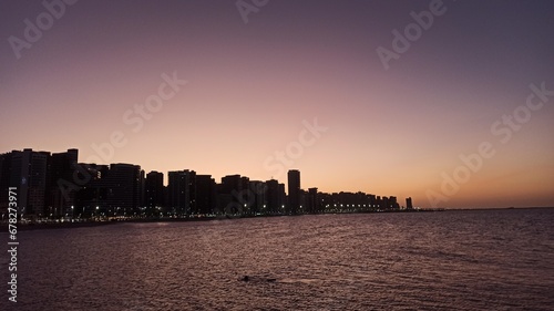 Beachfront twilight in Fortaleza; city lights and azure waves under a soft pink sky