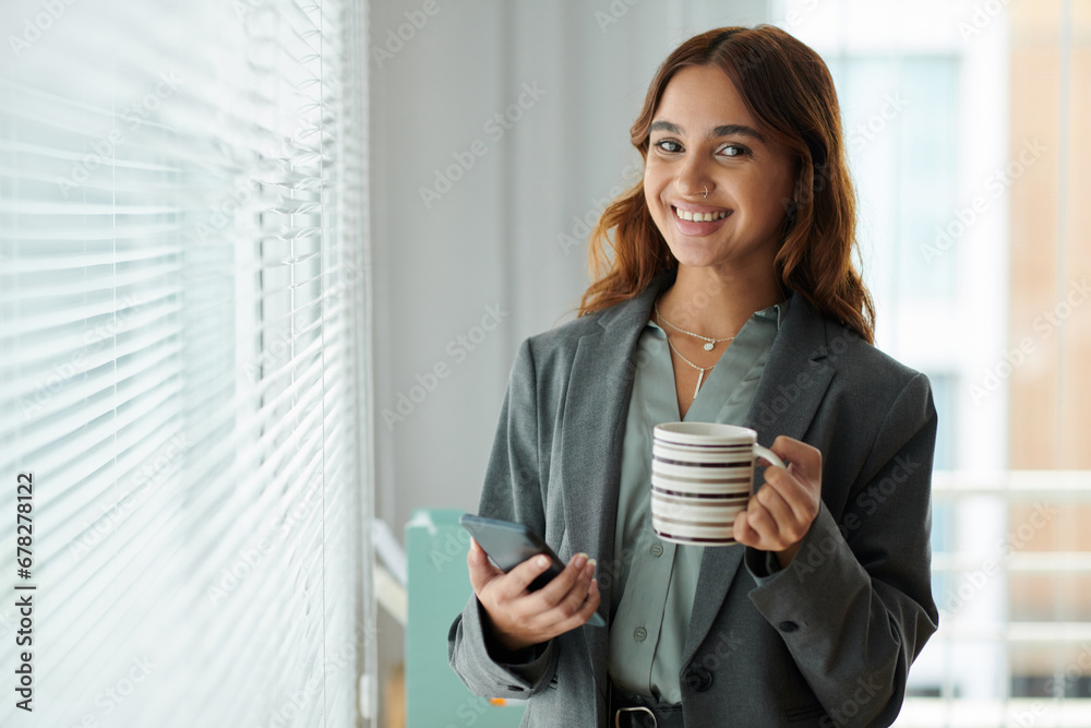 Portrait of happy smiling HR manager drinking cup of coffee and checking notifications on smartphone Portrait of happy smiling HR manager drinking cup of coffee and checking notifications on smartphone