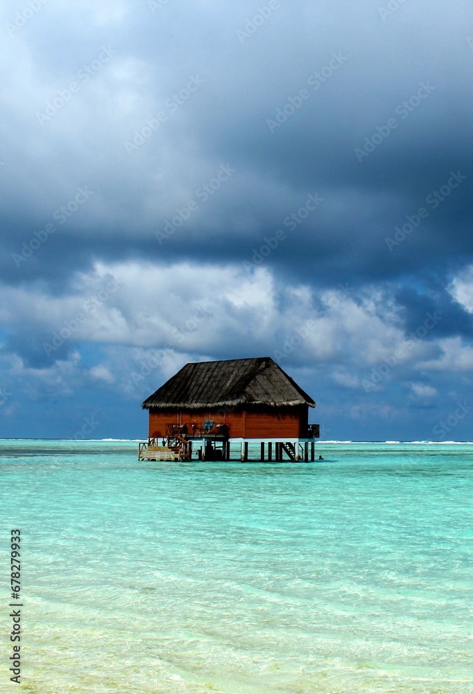 Hut on a beach in the Maldives surrounded by the bright blue waters of an ocean under a cloudy sky