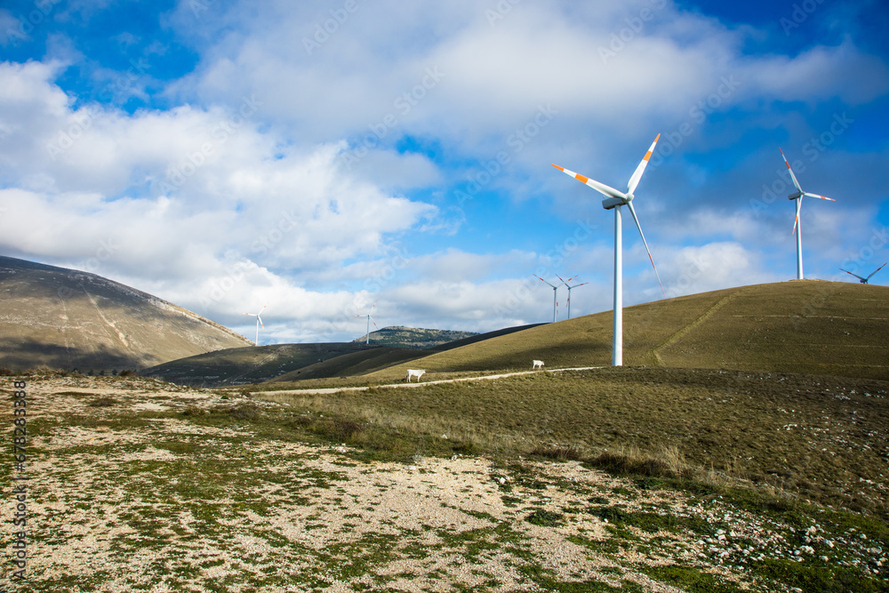 Wind farm with turbines on the mountains. Eco-sustainable industry with nature-friendly technologies for clean energy in a better environment. Conceptual mountainous landscape animals Wind farm with turbines on the mountains. Eco-sustainable industry with nature-friendly technologies for clean energy in a better environment. Conceptual mountainous landscape animals