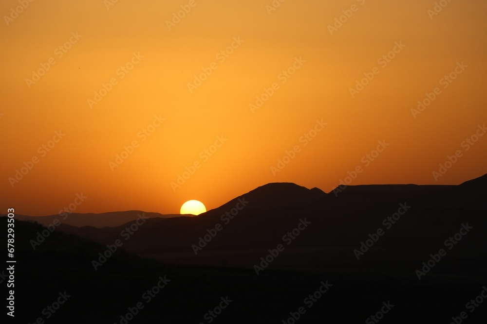 Of hills with an orange sun setting in the background