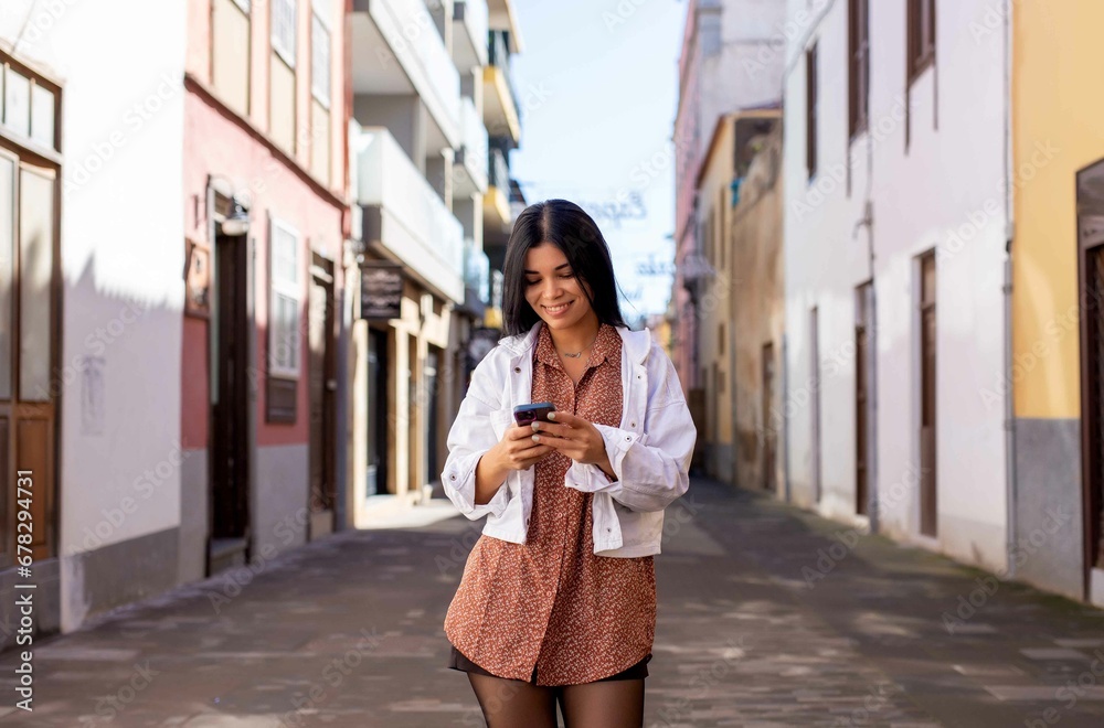 Happy Hispanic woman using mobile phone in town