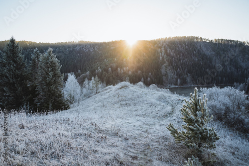 Morning sunrise on the mountain, the glare of the sun shining directly into the camera, the winter landscape, the first snow in the mountains, the hilly terrain, the ground covered with frost.