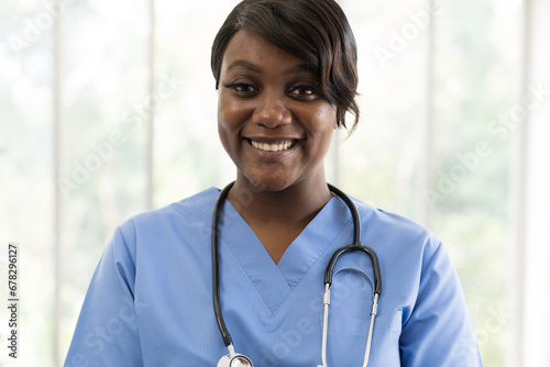 Closeup of happy and smiling African American young female doctor wearing blue scrubs uniform and stethoscope and standing at hospital © amorn