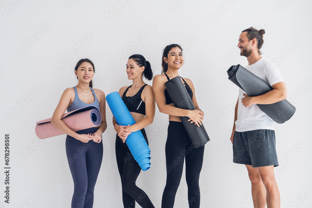 Obraz premium Group of male and female friends with yoga instructor standing holding yoga mats and talking after break, exercising, doing yoga, class in studio.Healthy lifestyle and wellness concept