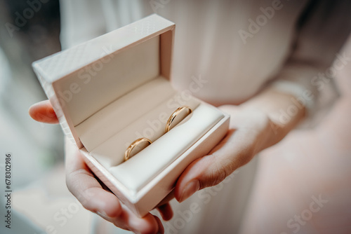 Due fedi nuziali in una scatola bianca per gioielli con un cuscino offerti dalle mani di una giovane donna photo