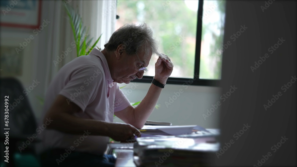 Candid senior man working at home inspecting documents concentrated reading paperwork. Older person in office desk Candid senior man working at home inspecting documents concentrated reading paperwork. Older person in office desk