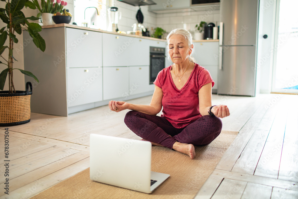 Senior woman practicing yoga in front of laptop at home Senior woman practicing yoga in front of laptop at home