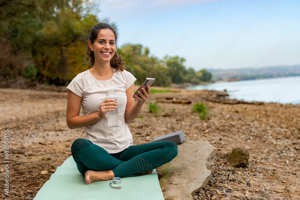 In between exercises, she uses her phone to remind herself of the next moves while sitting on a workout mat by the river on the beach.