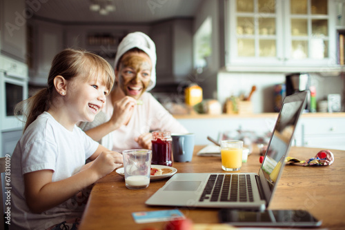 Little daughter using laptop with mother on dining table during breakfast at home