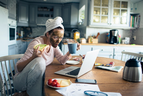 Young woman eating healthy breakfast in the morning using laptop at home