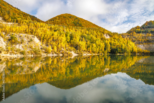 Autumn landscape with reflection of colorfull hills in the lake. Flooded quarry near the village Sutovo in Slovakia, Europe.
