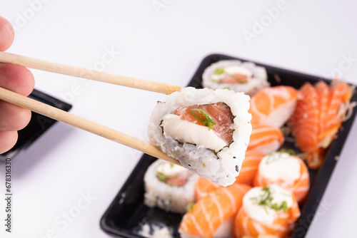 holding a piece of sushi with chopsticks with a tray of oriental food in the background