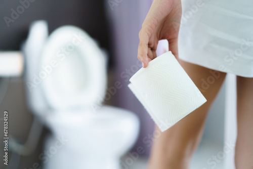 Asian young woman having a stomachache and food poisoning and getting to the toilet or restroom. Woman pick up a roll of tissue paper to the toilet.