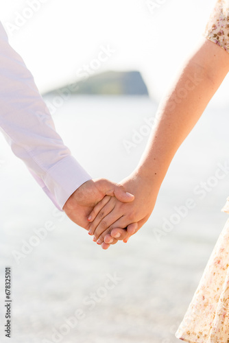 Man holds woman hand while standing on the seashore. Cropped. Faceless