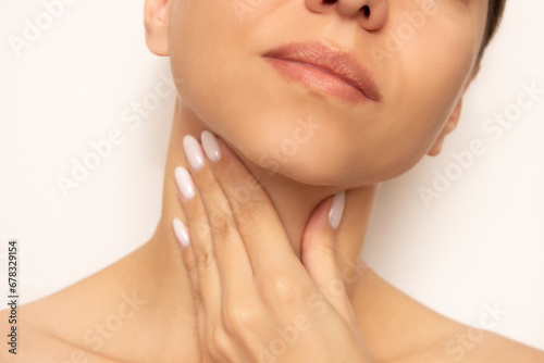 A young Caucasian woman frowns and puts her hand to her throat. Colds, flu, sore throat and ligaments, laryngitis, pharyngitis, tonsillitis. Discomfort, soreness and dryness in the throat close-up.