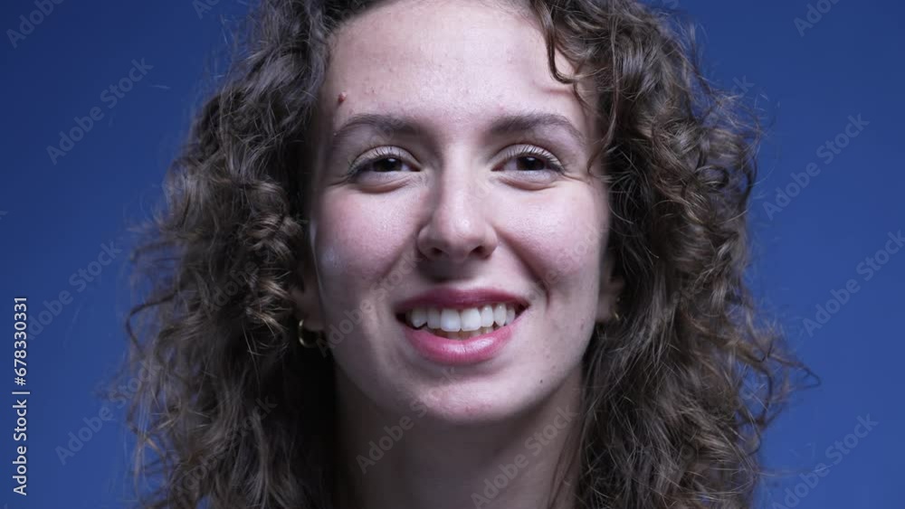 Happy woman close-up face smiling on blue backdrop. Portrait of a joyful female person in 20s looking at camera Happy woman close-up face smiling on blue backdrop. Portrait of a joyful female person in 20s looking at camera