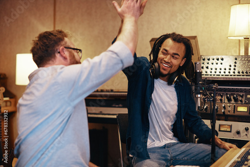 Smiling singer and producer high fiving together in a studio photo