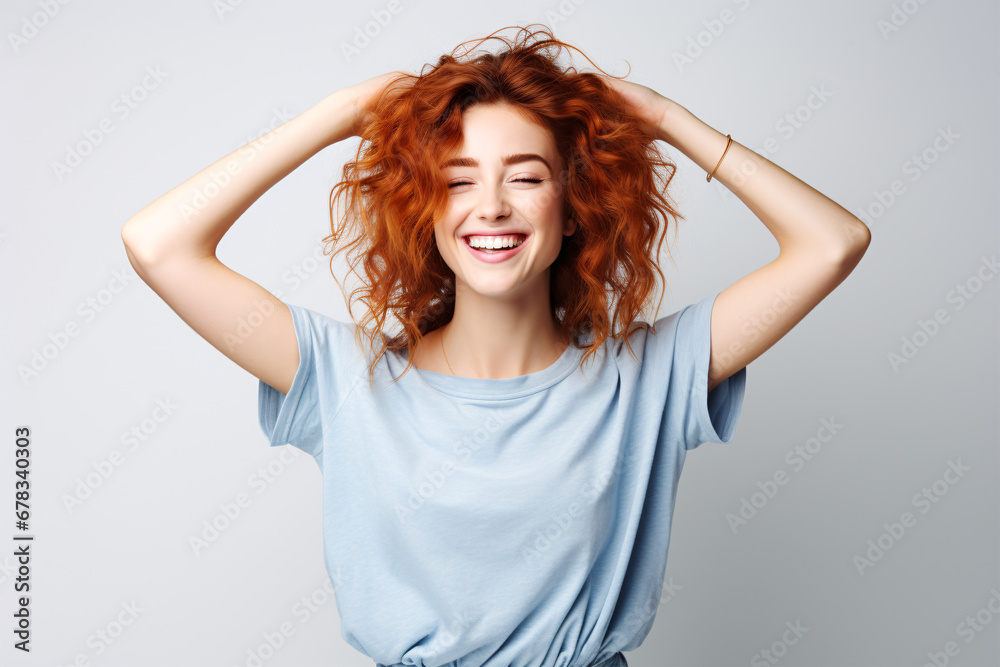 A cheerful redhead in a blue tee-shirt and jeans, dancing in elation with eyes shut, isolated against a white backdrop.