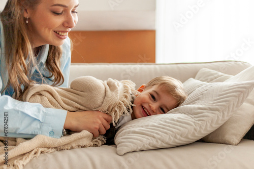 young mother hugs and covers her son with warm blanket on the sofa before going to bed, woman takes care of the child