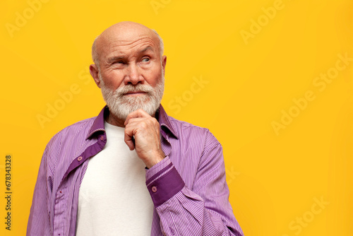 puzzled old bald grandfather in purple shirt with raised eyebrow plans and thinks on yellow isolated background