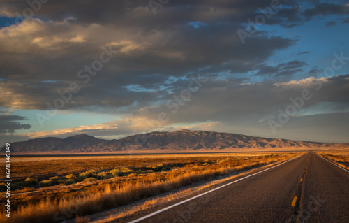 long straight desert road during sunset  Image shows the road in the Nevada desert during the golden hour giving off a beautiful scenic view of the desert and the mountains