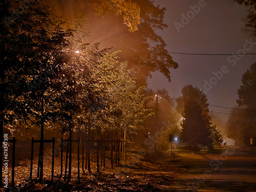 Street near Julianowski Park in Lodz lit with street lamps on a cloudy foggy autumn night, Lodz, Poland.