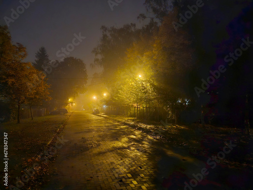 Street near Julianowski Park in Lodz lit with street lamps on a cloudy foggy autumn night, Lodz, Poland.