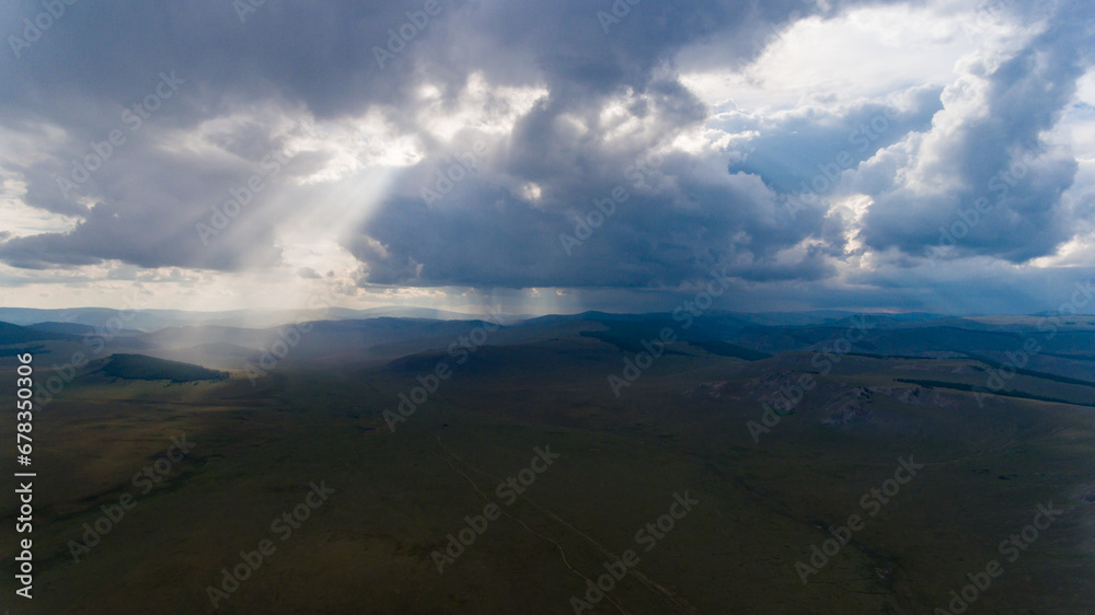 Sunrays piercing through clouds over Mongolian plains.