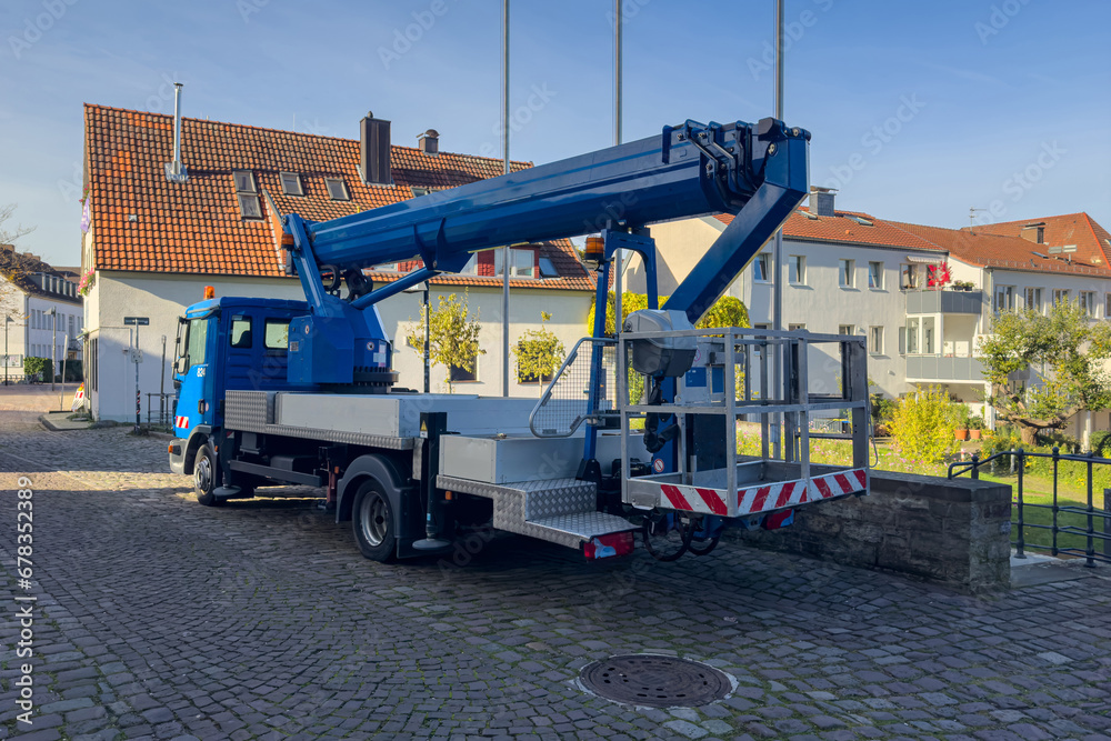 A blue car with a hydraulic lift for people stands on a paved sidewalk in front of residential buildings. A blue car with a hydraulic lift for people stands on a paved sidewalk in front of residential buildings.