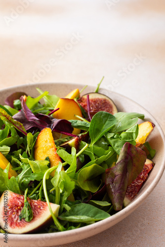 Salad with mixed lettuce and peaches with figs, plate with salad on beige background