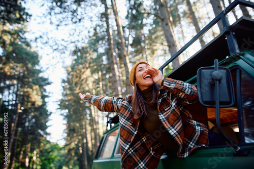 Cheerful woman has fun on journey while screaming through window of camper van in nature.