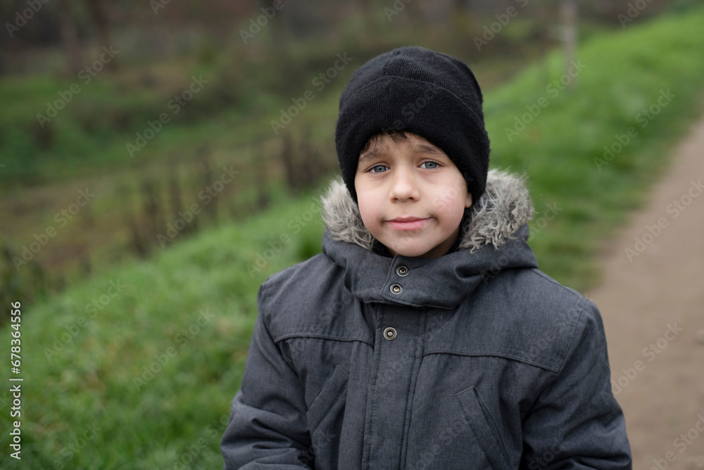 A young boy is warmly dressed during a walk in spring, he is already hot after active games in the fresh air, the boy is a little disappointed, he was waiting for dad and dad was late at work A young boy is warmly dressed during a walk in spring, he is already hot after active games in the fresh air, the boy is a little disappointed, he was waiting for dad and dad was late at work