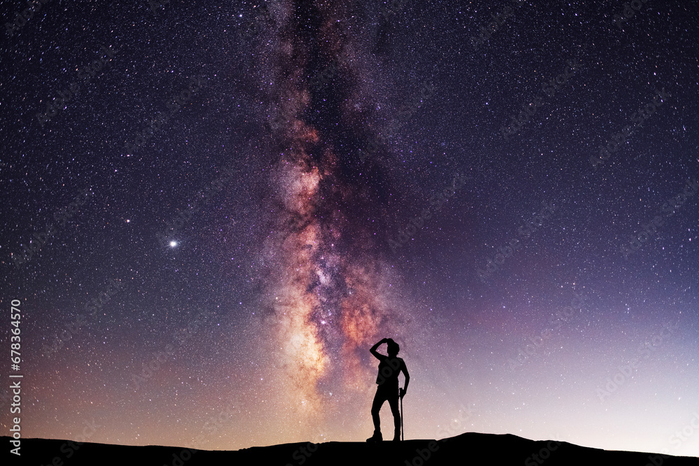 Silhouette of a hiker standing on the hill, on the milky way galaxy background. Cosmos wallpaper. 