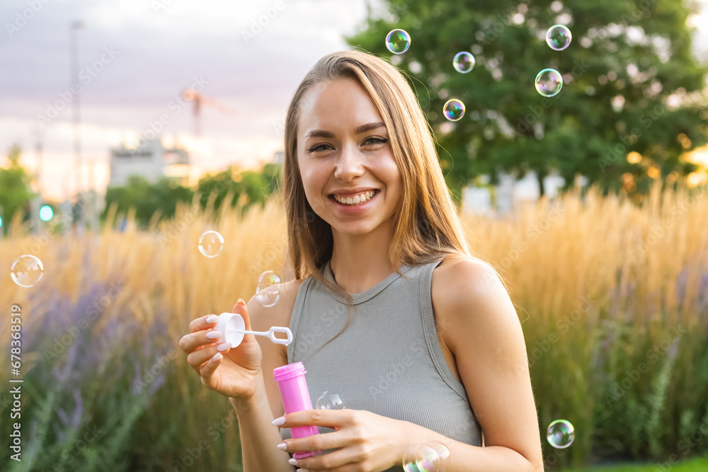A joyous young woman with long, flowing hair creates soap bubbles at sunset in the park.