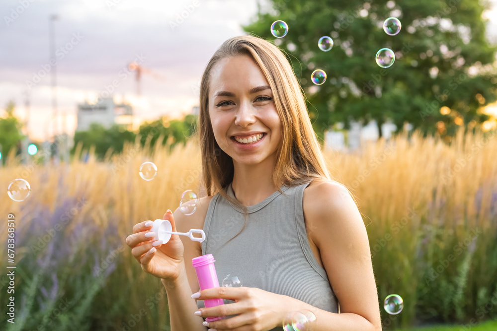 A joyous young woman with long, flowing hair creates soap bubbles at sunset in the park. A joyous young woman with long, flowing hair creates soap bubbles at sunset in the park.