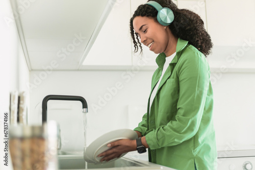 black lady in headphones enjoying music scrubbing plates in kitchen
