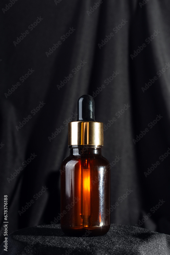 Brown bottle with dropper with a beauty serum on black background. Glass packaging for cosmetic product, essential aroma oil. Skin care, hydration and nutrition with collagen..
